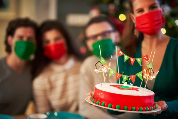 Grupo de amigos en máscaras celebrando la Navidad en casa con pastel de lujo —  Fotos de Stock