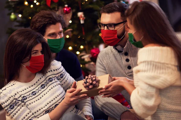 Grupo de amigos con máscaras que intercambian regalos de Navidad en casa —  Fotos de Stock