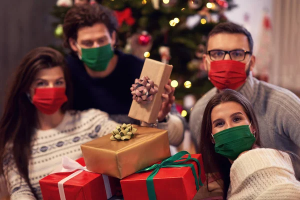 Grupo de amigos con máscaras que intercambian regalos de Navidad en casa —  Fotos de Stock