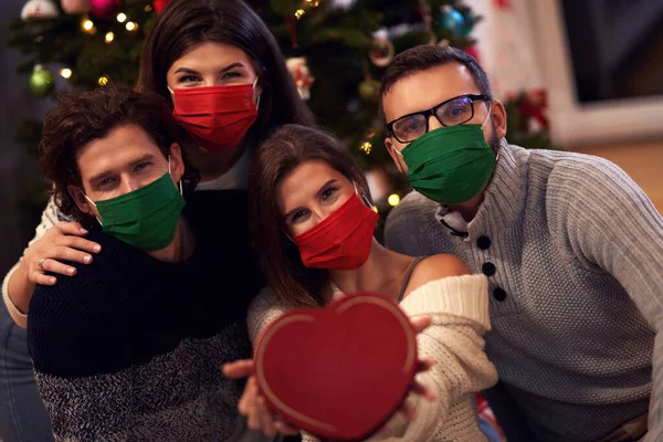 Grup de prieteni purtând măști care fac schimb de cadouri de Crăciun acasă — Fotografie, imagine de stoc