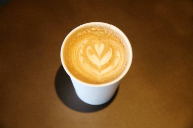 Masanın üzerine kalp latte resmi çizilmiş bir fincan kahve.