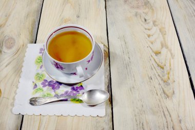 Çay dolu güzel bir çay fincanı mavi çiçekli bir peçeteye yerleştirilir. Üzerinde güzel bir çay kaşığı var..