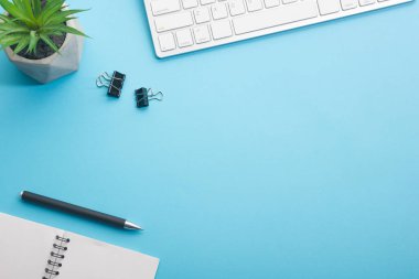 Dizüstü bilgisayarı, akıllı telefonu ve bir fincan kahveli diğer iş malzemeleri olan mavi masa ofisi. Metni kopyalamak için üst görünümü kullan. Desenci çalışma alanı düz masa üzerinde temel elementler yatıyordu