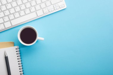 Dizüstü bilgisayarı, akıllı telefonu ve bir fincan kahveli diğer iş malzemeleri olan mavi masa ofisi. Metni kopyalamak için üst görünümü kullan. Desenci çalışma alanı düz masa üzerinde temel elementler yatıyordu