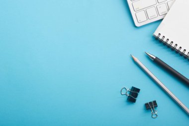 Dizüstü bilgisayarı, akıllı telefonu ve bir fincan kahveli diğer iş malzemeleri olan mavi masa ofisi. Metni kopyalamak için üst görünümü kullan. Desenci çalışma alanı düz masa üzerinde temel elementler yatıyordu