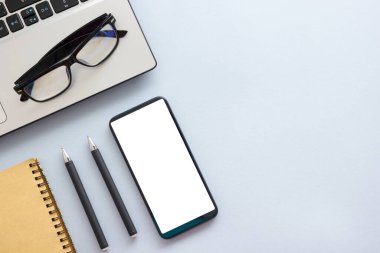 Dizüstü bilgisayarı, akıllı telefonu ve bir fincan kahveli diğer iş malzemeleri olan mavi masa ofisi. Metni kopyalamak için üst görünümü kullan. Desenci çalışma alanı düz masa üzerinde temel elementler yatıyordu