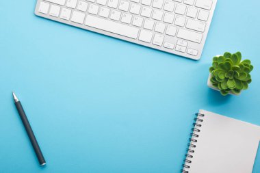 Dizüstü bilgisayarı, akıllı telefonu ve bir fincan kahveli diğer iş malzemeleri olan mavi masa ofisi. Metni kopyalamak için üst görünümü kullan. Desenci çalışma alanı düz masa üzerinde temel elementler yatıyordu
