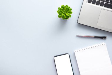 Dizüstü bilgisayarı, akıllı telefonu ve bir fincan kahveli diğer iş malzemeleri olan mavi masa ofisi. Metni kopyalamak için üst görünümü kullan. Desenci çalışma alanı düz masa üzerinde temel elementler yatıyordu