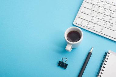 Dizüstü bilgisayarı, akıllı telefonu ve bir fincan kahveli diğer iş malzemeleri olan mavi masa ofisi. Metni kopyalamak için üst görünümü kullan. Desenci çalışma alanı düz masa üzerinde temel elementler yatıyordu
