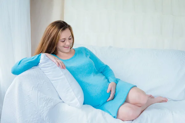 快乐的年轻孕妇休息在沙发上 拥抱和看在她的大肚子 — 图库照片