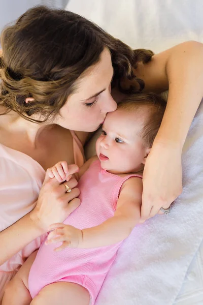 美丽的年轻妈妈抱着她4个月大的女婴在床上 快乐的母亲的概念 — 图库照片