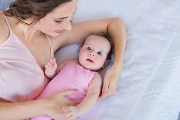 美丽的年轻妈妈抱着她4个月大的女婴在床上 快乐的母亲的概念 — 图库照片