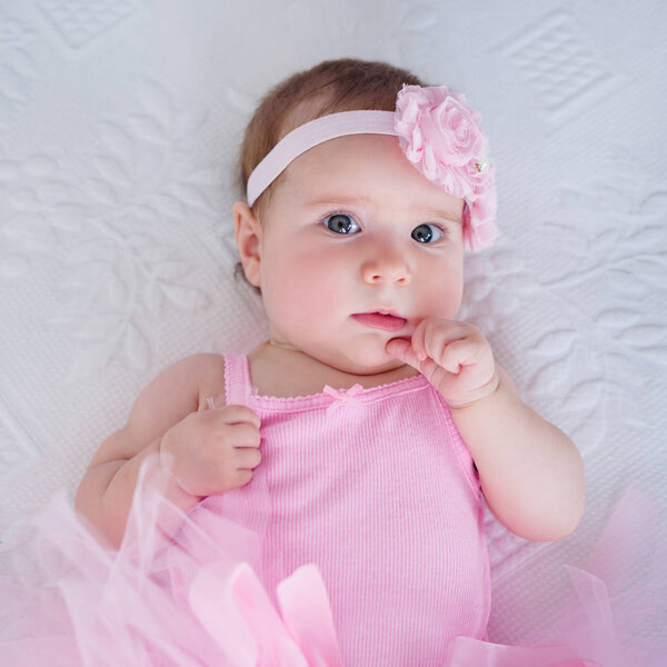 adorable baby girl 4 months old resting on the bed wearing pink headband and tutu dress