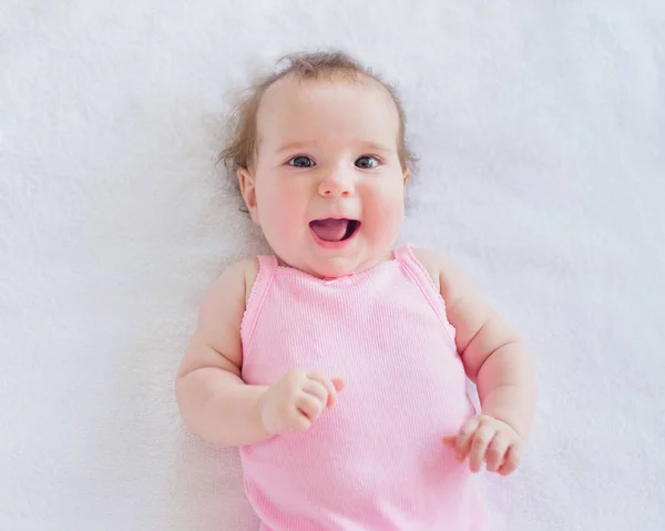 快乐笑女婴4个月大休息在床上观看在镜头里 快乐的童年概念 免版税图库照片