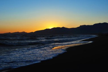Arka planda dağlar ile sahilde güzel gün batımı