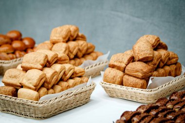 Puffs, turta ve beyaz kağıt peçeteye hasır sepetleri gri bir arka plan üzerinde beyaz bir masa örtüsü ile kaplı bir masada yatan choux hamur işleri kare