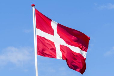 Flag of Denmark in red and white colors waving in the wind on a blue sky clipart