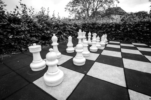 Game of chess with large pieces in an outdoor garden in monchrome colors