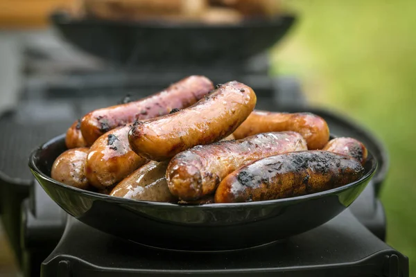 Grilled sausages on a plate at an outdoor barbecue kitchen with a stack of wieners