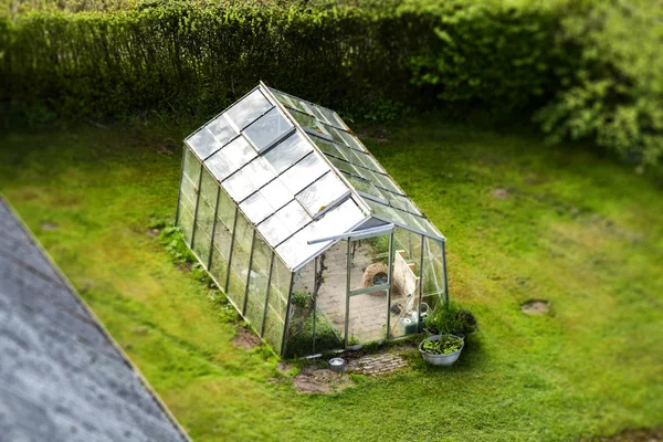 Green house with glass windows on a green lawn in the spring seen from above