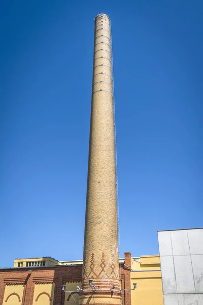 Tall chimney made of bricks on a factory under a blue sky