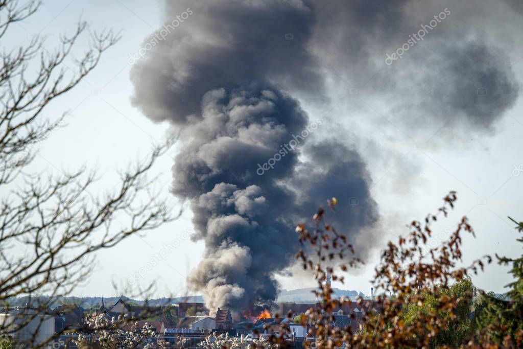 House on fire in a city with black smoke covering the sky in the daytime