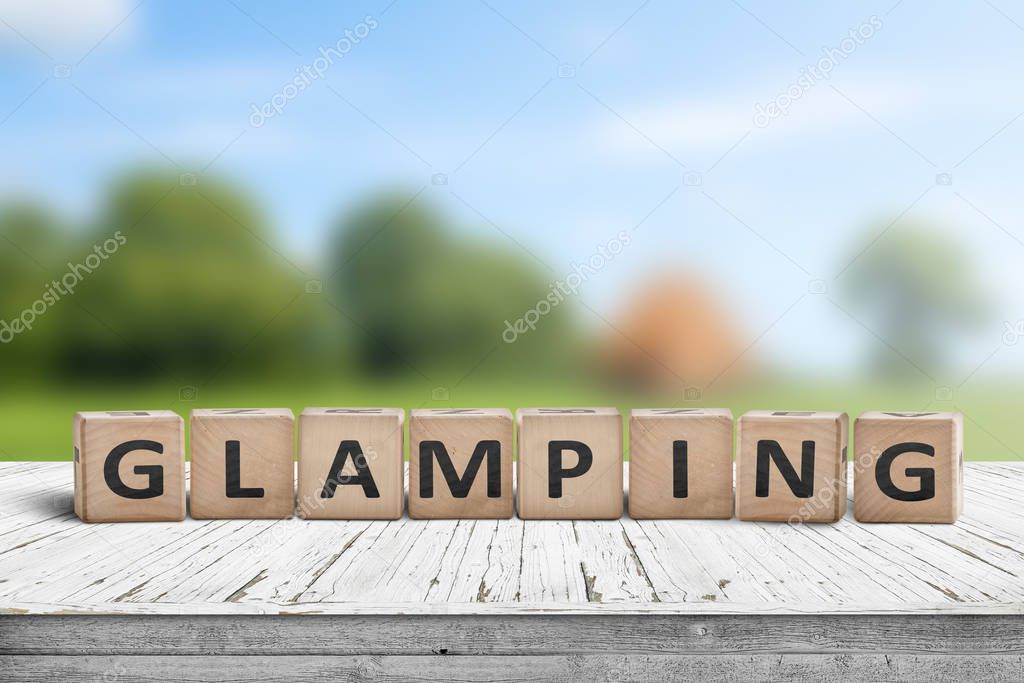 Glamping sign on wooden planks in the summer with a green camping area in the background
