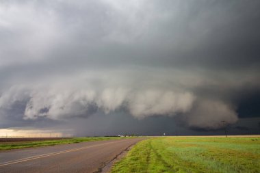A big supercell storm with a shelf cloud and a wall cloud looms over a road in the rural countryside. clipart