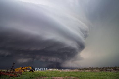 A huge supercell storm with a ground scraping wall cloud fills the sky over Nebraska farmland. Striations can be seen in its massive rotating updraft. clipart