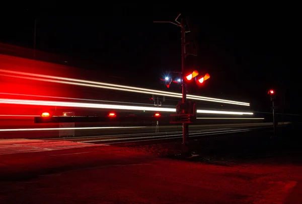 A train in the night creates a streak of lights as it crosses a country road in rural America.