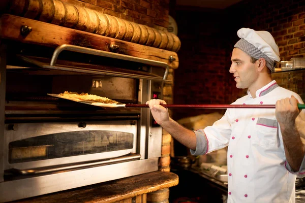 Food concept. Preparing traditional italian pizza. Young chef in white uniform holds in his hands shovel for pizza