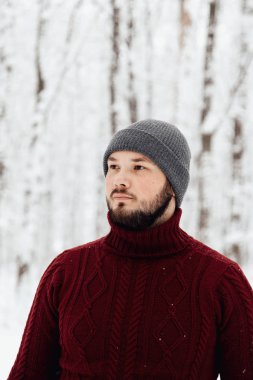 adam kırmızı örgü kazak ve kış ormanın içinde kar üzerinde duran bir telefon tutarak kot