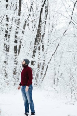 adam kırmızı örgü kazak ve kış ormanın içinde kar üzerinde duran bir telefon tutarak kot