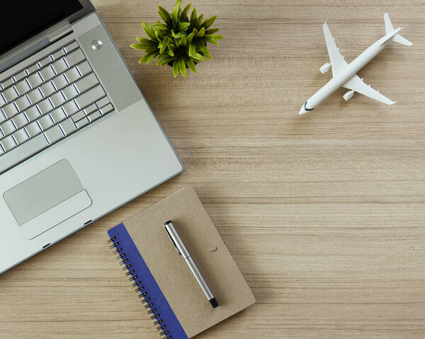 Office wood table with notepad and airplane, computer and tree. top view with copy space for design. flat lay