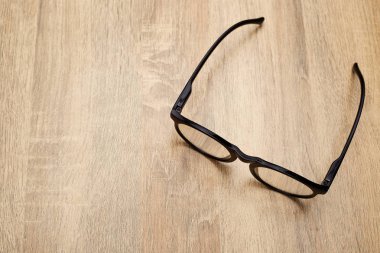 Ahşap arka planda siyah çerçeveli gözlükler, masa. Yukarıdan görüntüle.
