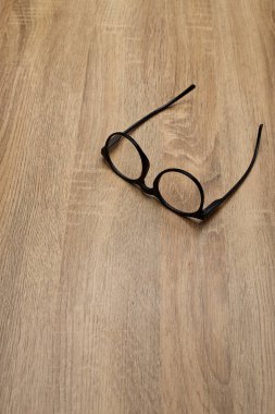 Ahşap arka planda siyah çerçeveli gözlükler, masa. Yukarıdan görüntüle.