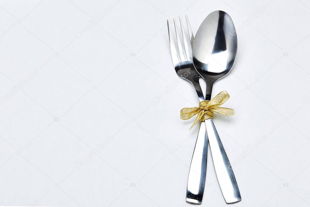 Fork and spoon with gold ribbon on white background