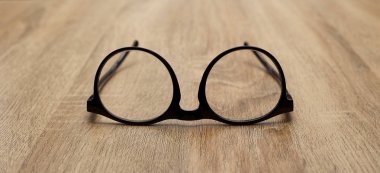 Ahşap arka planda siyah çerçeveli gözlükler, masa. Yukarıdan görüntüle.