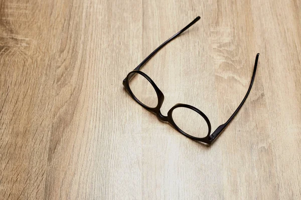 Ahşap arka planda siyah çerçeveli gözlükler, masa. Yukarıdan görüntüle.