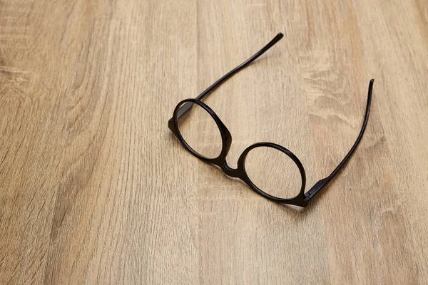 Ahşap arka planda siyah çerçeveli gözlükler, masa. Yukarıdan görüntüle.