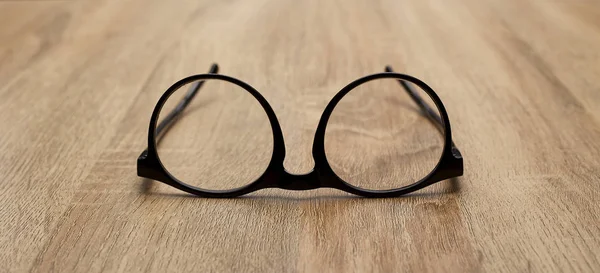 Ahşap arka planda siyah çerçeveli gözlükler, masa. Yukarıdan görüntüle.