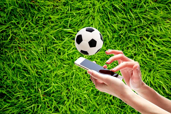 フィールド上にサッカー ボールに対してスマート フォンを持っている手のクローズ アップ — ストック写真