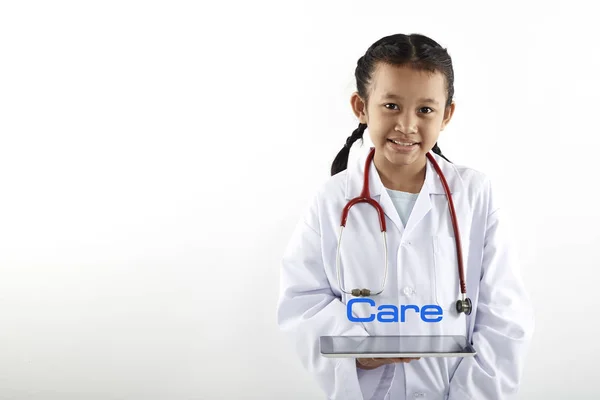 可爱的亚洲小女孩在医生服装与听诊器和平板电脑微笑着 看着远离白色背景 医疗保健概念 — 图库照片