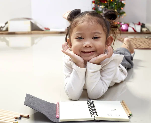 children of girl with smiles on their faces and in good spirits dream of New Year gifts and write wishes for Santa Claus with pen on paper and pose on camera.