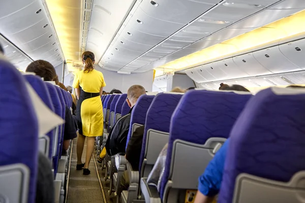 blurred Interior of commercial airplane with flight attandant serving passengers on seats during flight. Stewardess in dark Yellow uniform walking the aisle. Horizontal composition.