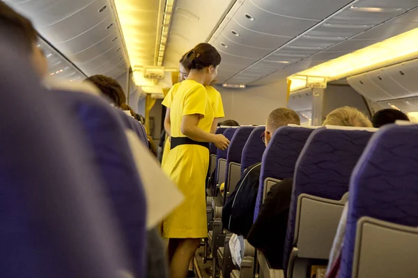 blurred Interior of commercial airplane with flight attandant serving passengers on seats during flight. Stewardess in dark Yellow uniform walking the aisle. Horizontal composition.