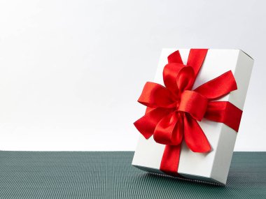 Kırmızı kurdele hediye kutusu yeşil bir arka plan üzerine yerleştirilir. Beyaz arka tasarım güneş ışığı alan soldan geliyor. Festivaller için hediye fikirleri