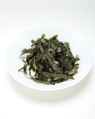 Beyaz bir tablo üzerinde beyaz bir tabak içinde kurutulmuş yosun mühür. Tasarım alanı olan doğal ışık ışık öykünür.