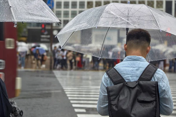 渋谷の正方形で雨の中歩いて傘を持つ男 — ストック写真
