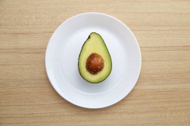 Sağlıklı Vejetaryen, kahverengi ahşap masa üzerinde beyaz plaka üzerinde avokado.